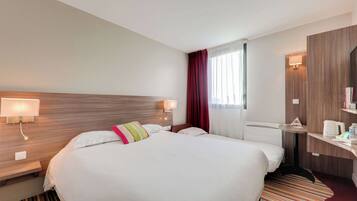 Habitación de hotel con una cama grande, dos lámparas de noche, un cabecero de madera, un escritorio pequeño con una lámpara, una cafetera y un tapete a rayas.