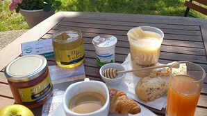 Montaje para picnic con comida y bebidas sobre una mesa de madera, incluyendo un croissant, manzana, dosificador de miel y un vaso de jugo.