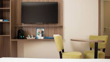 Une chambre d’hôtel équipée d’un téléviseur à écran plat fixé au mur, d’une machine à café et d’une petite table avec deux chaises jaunes.