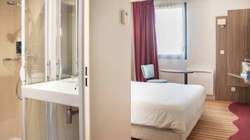 Une chambre d’hôtel avec une douche, un lit, une petite table et une fenêtre avec des rideaux.