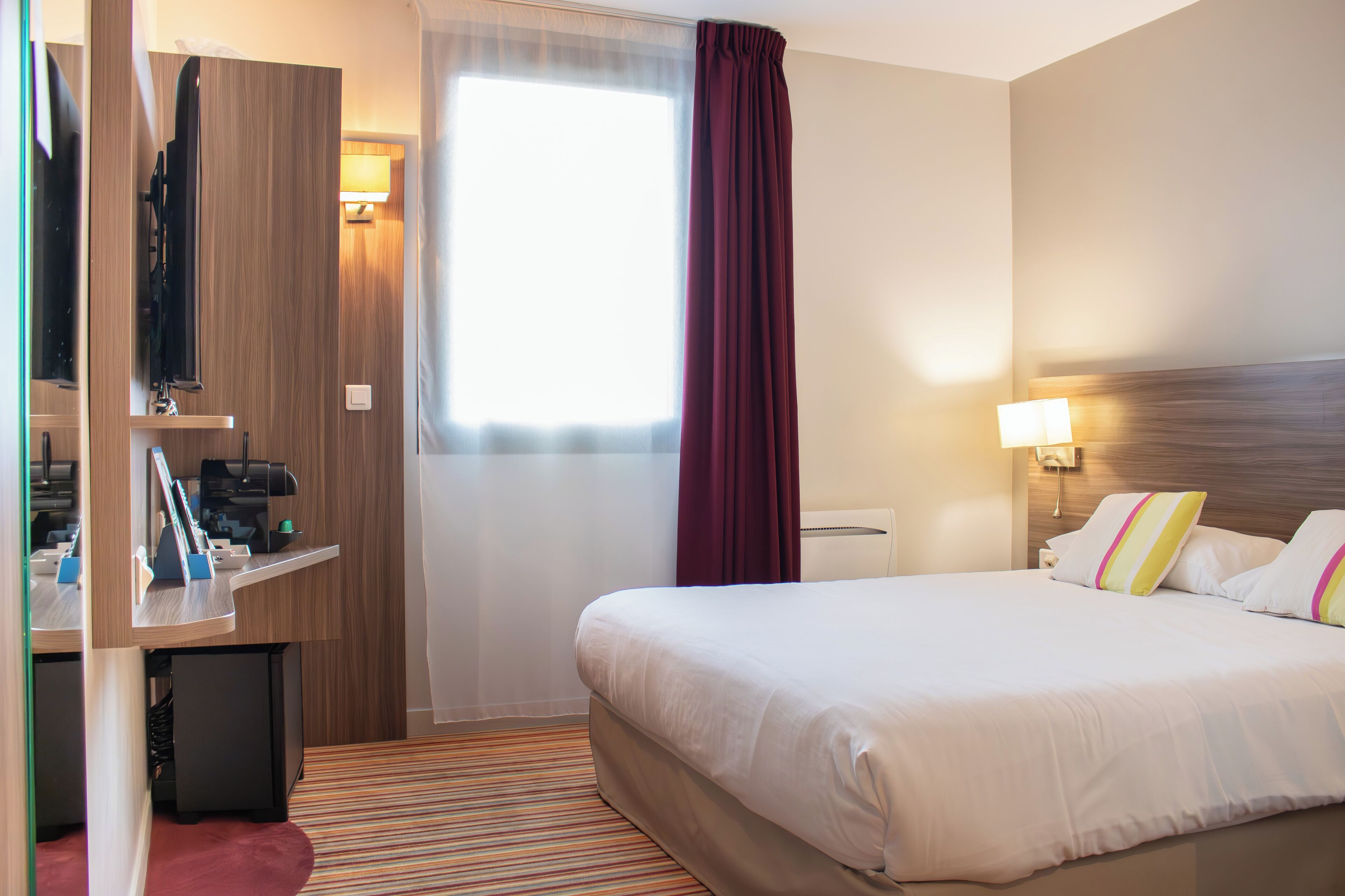 Een hotelkamer met een groot bed, een bureau met een computer, een televisie en een raam met gordijnen.