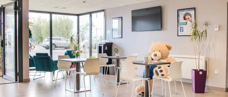 Un área de espera moderna con sillas color turquesa, un gran oso de peluche y una máquina de café.