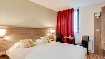 Habitación de hotel con una cama grande, dos lámparas de noche, una mesita, una silla y un ventanal con cortinas rojas.