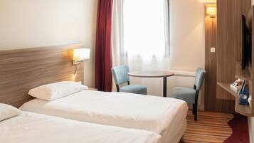 Une chambre d’hôtel avec deux lits, une petite table, deux chaises, un téléviseur et une fenêtre avec des rideaux.