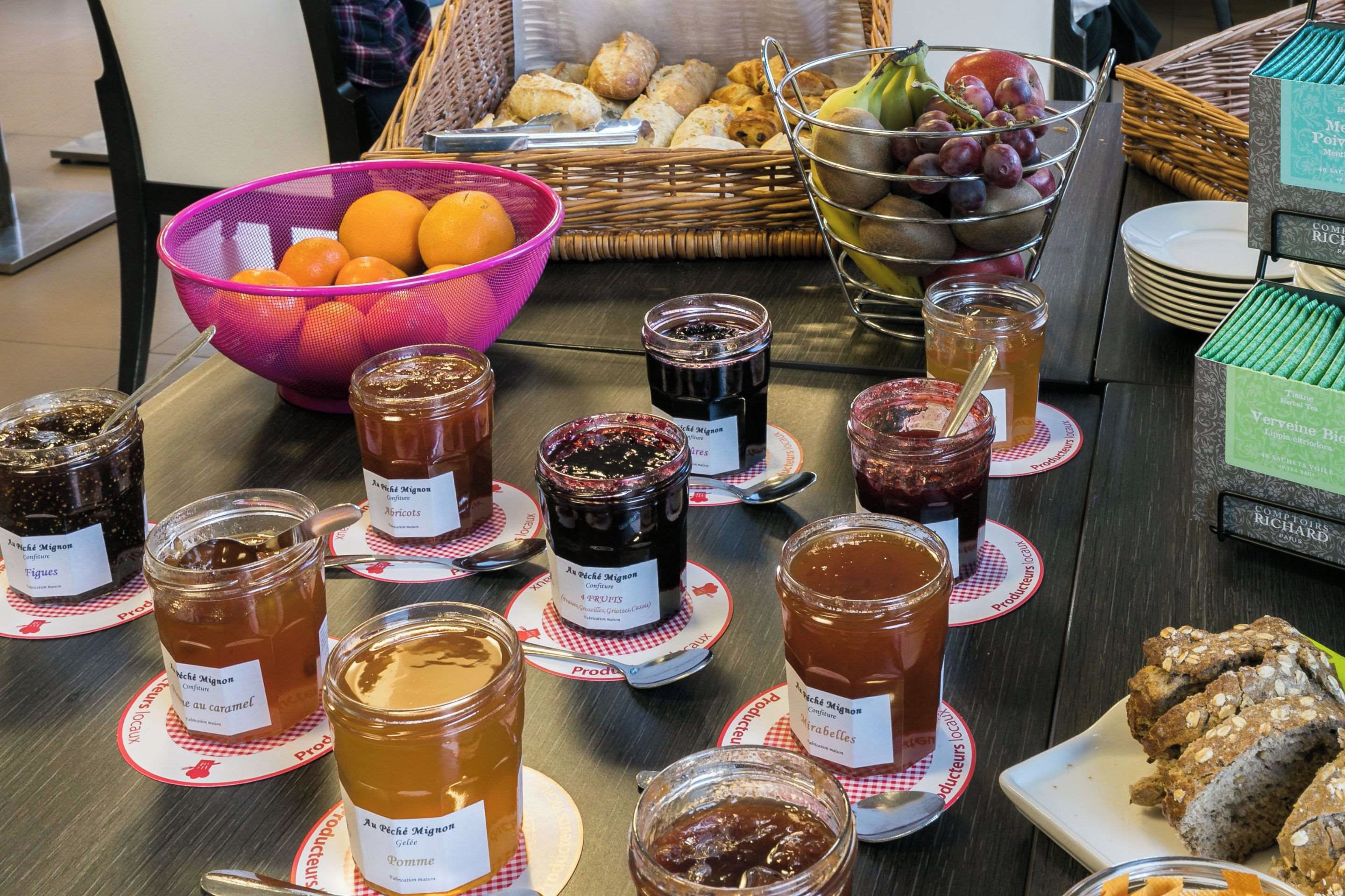 Una mesa con botes de conservas variados y una cesta de frutas.