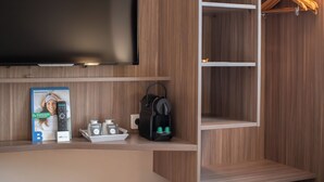Habitación de hotel con televisor de pantalla plana, un mueble para revistas con control remoto, una cafetera y una bandeja con tazas.