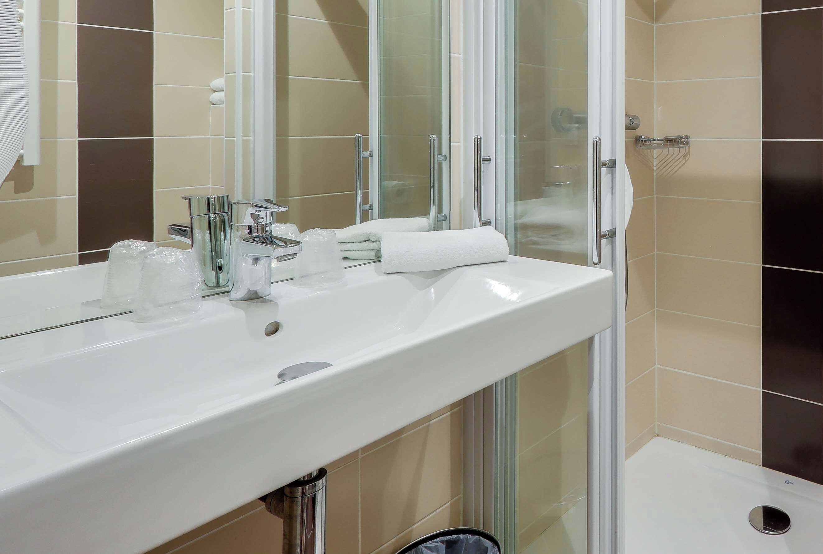 A bathroom with a white sink, glass shower enclosure, and beige tiles.