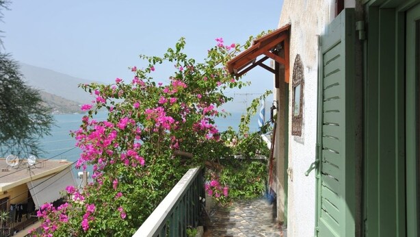 A balcony with a view of the sea, a wooden pergola, and a building with green shutters. - Elounda Apartments (Agios Nikolaos)