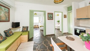 A cozy room with a green sofa, a small table, and a kitchen area with cabinets and a stove. - Elounda Apartments (Agios Nikolaos)