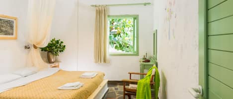 A bedroom with a bed, a window with a view of greenery, a chair, and a green door.