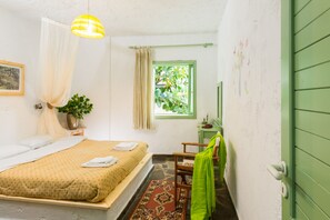 A bedroom with a bed, a window with a view of greenery, a chair, and a green door. - Elounda Apartments (Agios Nikolaos)