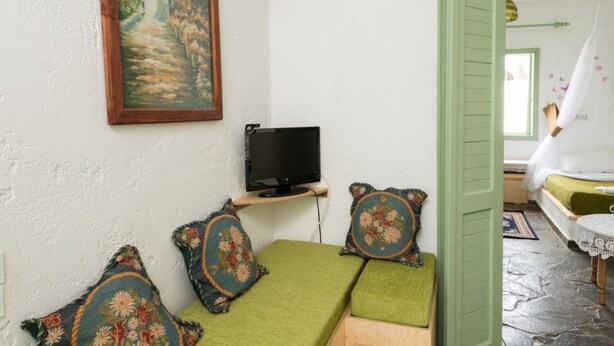 A cozy room with a green sofa, a television on a wooden stand, and a painting on the wall. - Elounda Apartments (Agios Nikolaos)