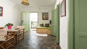 A room with a stone floor, a wooden table with chairs, a green door, a bench with cushions, and a hanging light fixture. - Elounda Apartments (Agios Nikolaos)