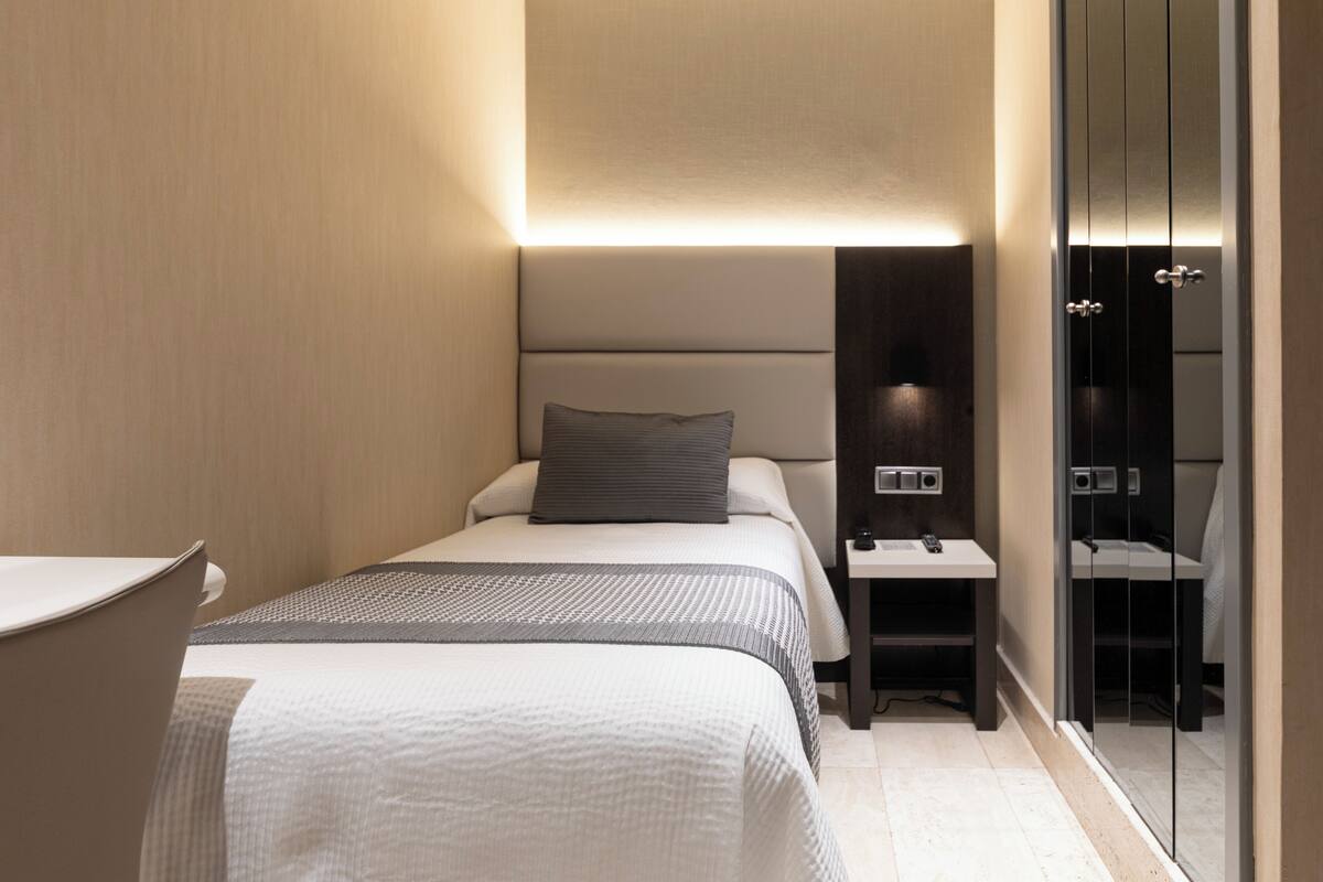 Quarto de hotel moderno com cama bem arrumada, mesa de cabeceira com abajur e um espelho grande.