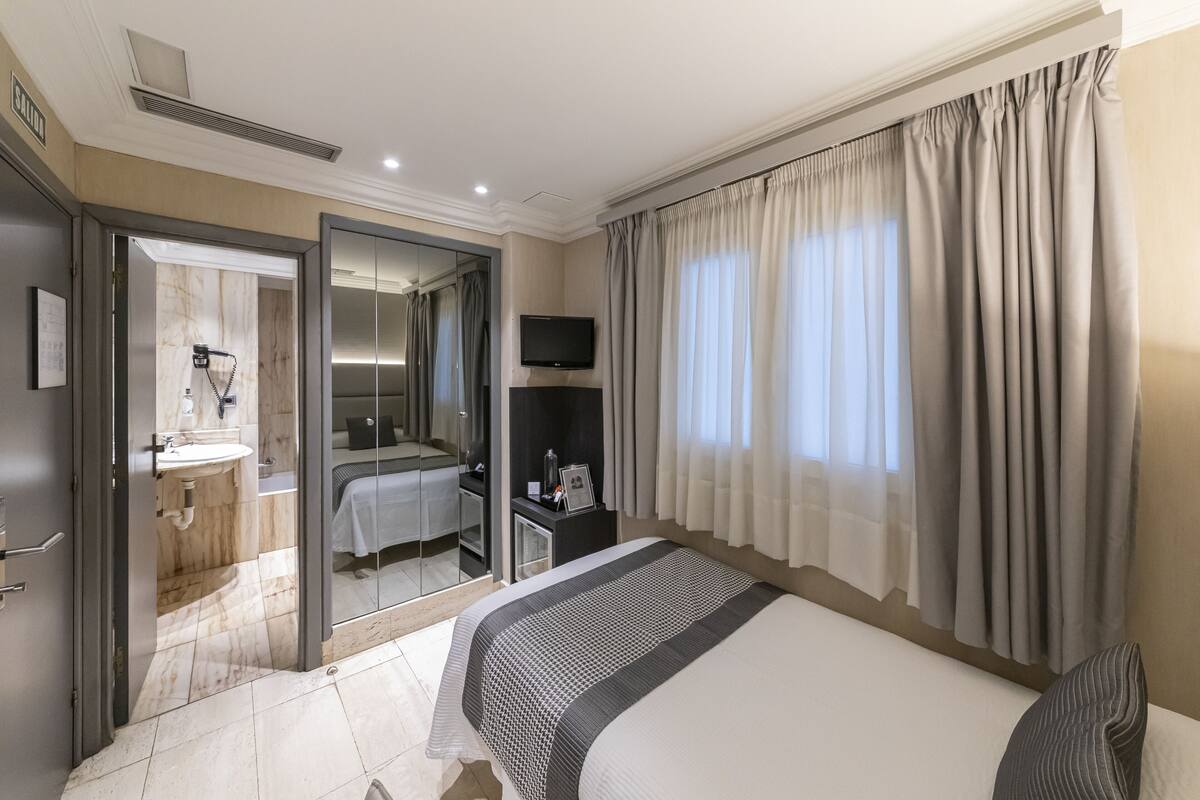 Quarto de hotel com cama grande, televisão, escrivaninha e banheiro visível por uma porta aberta.
