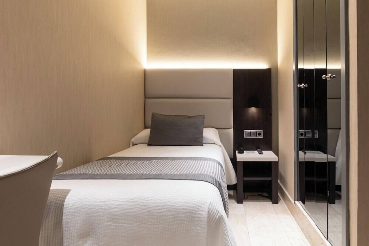 Quarto de hotel moderno com cama, mesa de cabeceira e espelho.