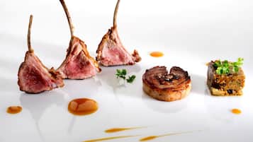 Un plat blanc amb tres entrecot de xai, una carn a la planxa i un bol petit amb verdures i salsa.