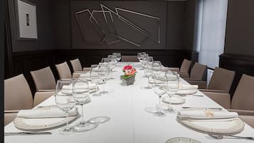 A long dining table set for a formal meal with multiple chairs, a centerpiece, and a modern wall design.
