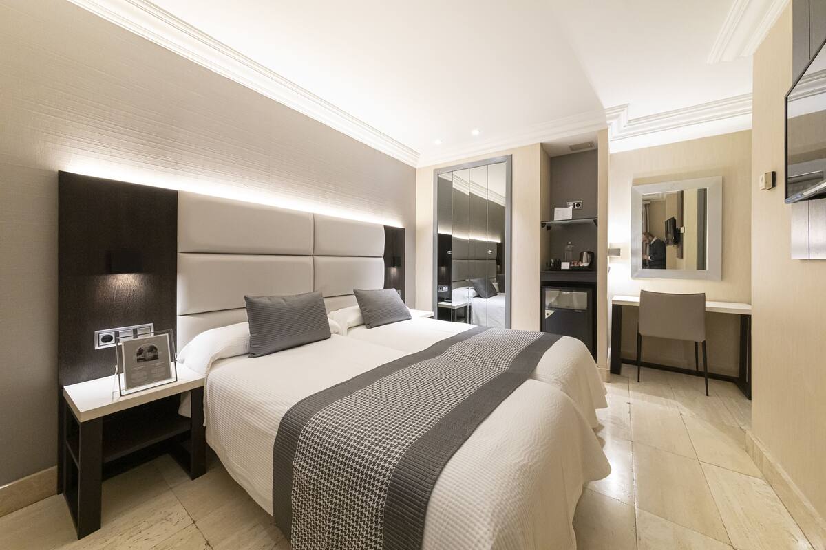 Quarto de hotel moderno com uma cama grande, mesa de cabeceira e escrivaninha com cadeira.