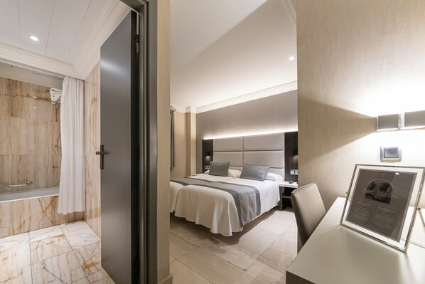 Una habitación de hotel moderna con baño de mármol, una cama bien hecha y una mesita de noche con un cuadro enmarcado.