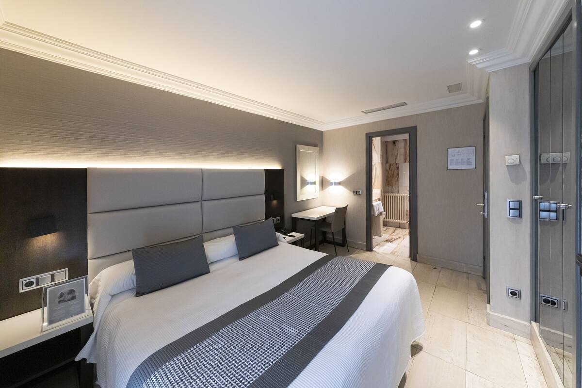 Quarto de hotel moderno com uma cama grande, mesas de cabeceira, uma escrivaninha e um espelho.