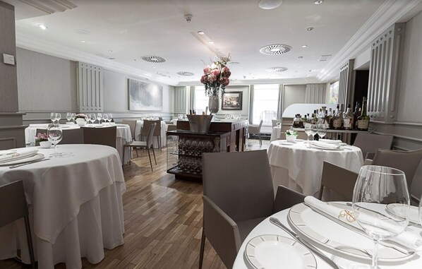 Un comedor amplio con mesas redondas, manteles blancos y un arreglo floral central.