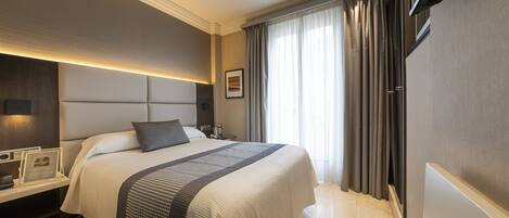 A modern hotel room with a large bed, bedside tables, a flat-screen TV, and a large window with curtains.