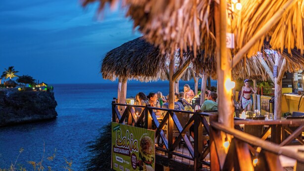 Un restaurante frente a la playa con techos de paja y estructuras de madera, con vistas al océano.
