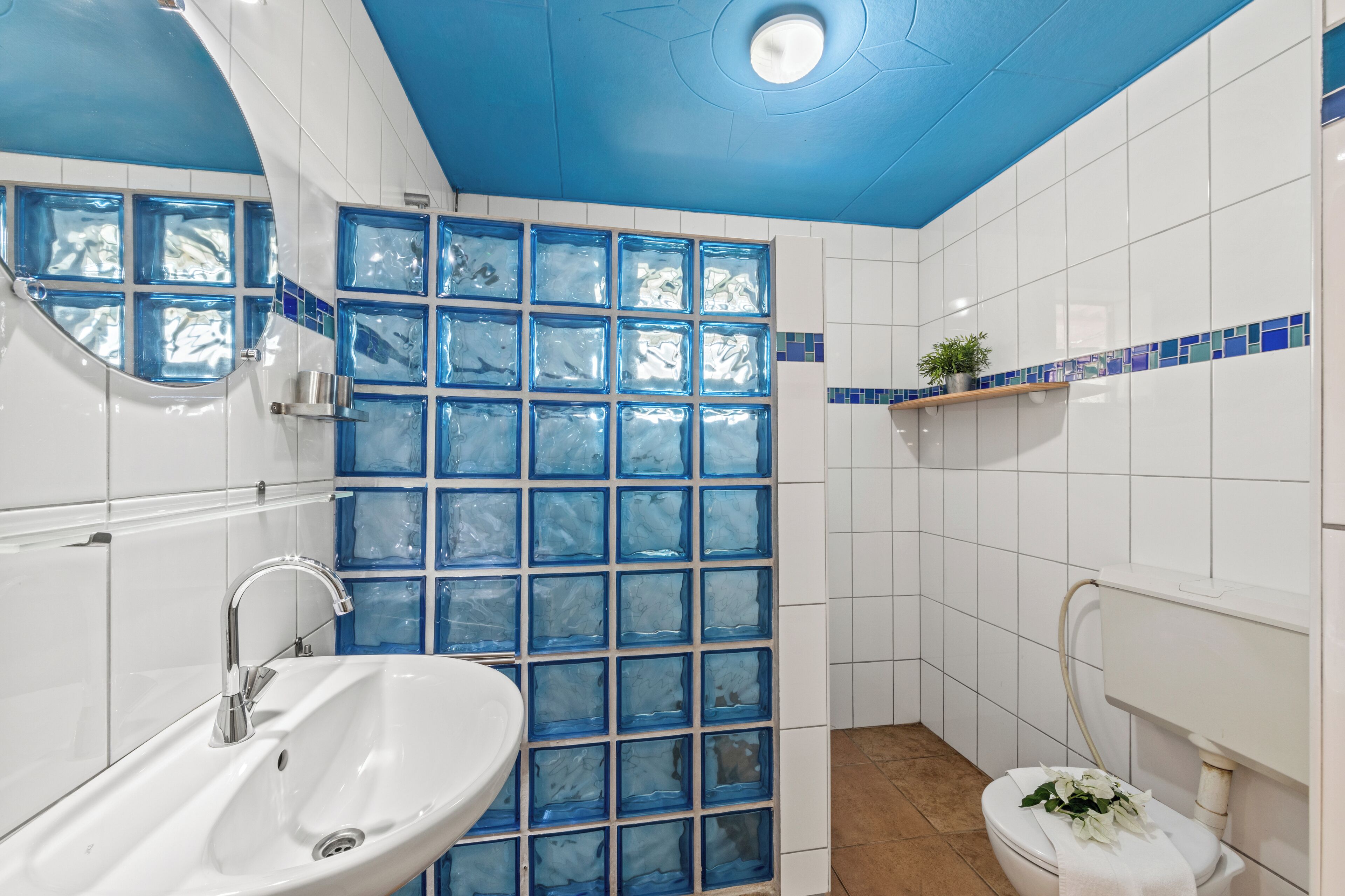A bathroom with a white sink, blue-tiled shower enclosure, and a toilet with a white toilet paper holder.