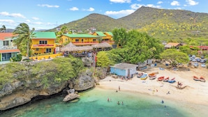Un resort costero con edificios coloridos, una playa con barcos y aguas turquesas cristalinas.