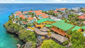 A coastal resort with colorful buildings, a thatched-roof restaurant, and clear blue waters.