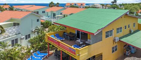 A multi-story building with a green roof, a balcony with blue lounge chairs, and a view of the ocean.