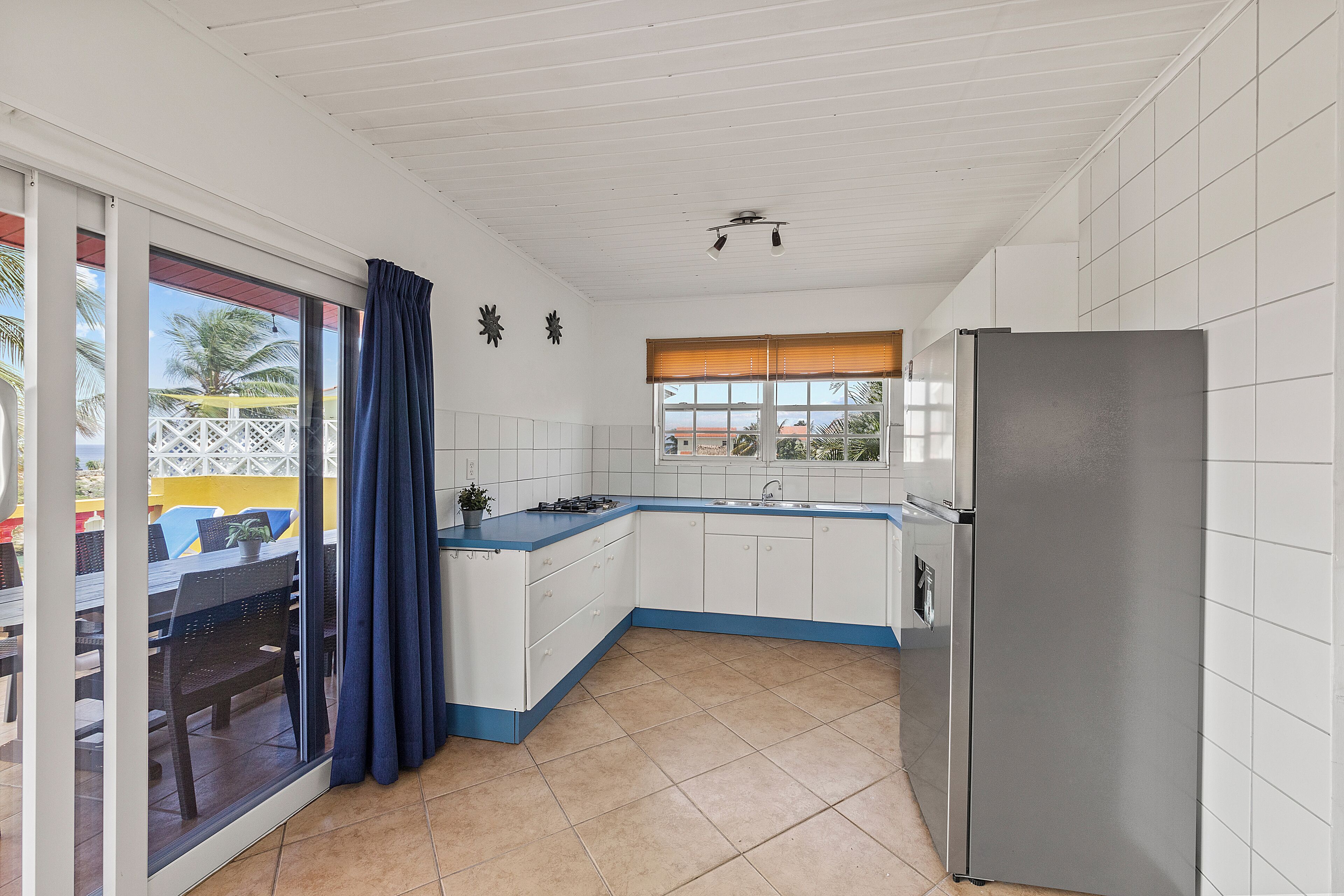 A compact kitchen with white cabinets, a stainless steel refrigerator, and a window with blinds.