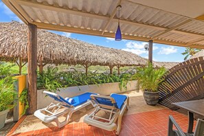 A covered outdoor area with two lounge chairs, a wooden table, and a thatched roof structure.