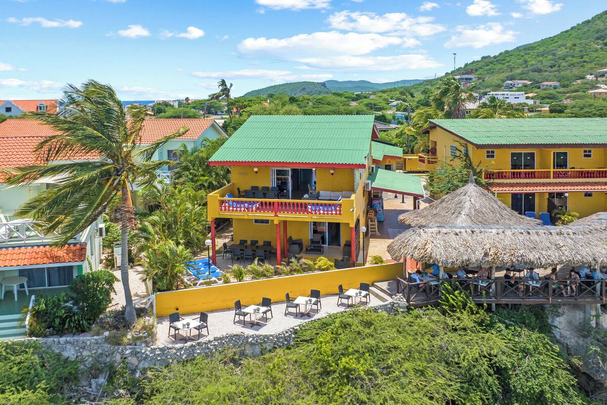 Un hotel costero con varias edificaciones, piscina y zona de bar con techo de paja.