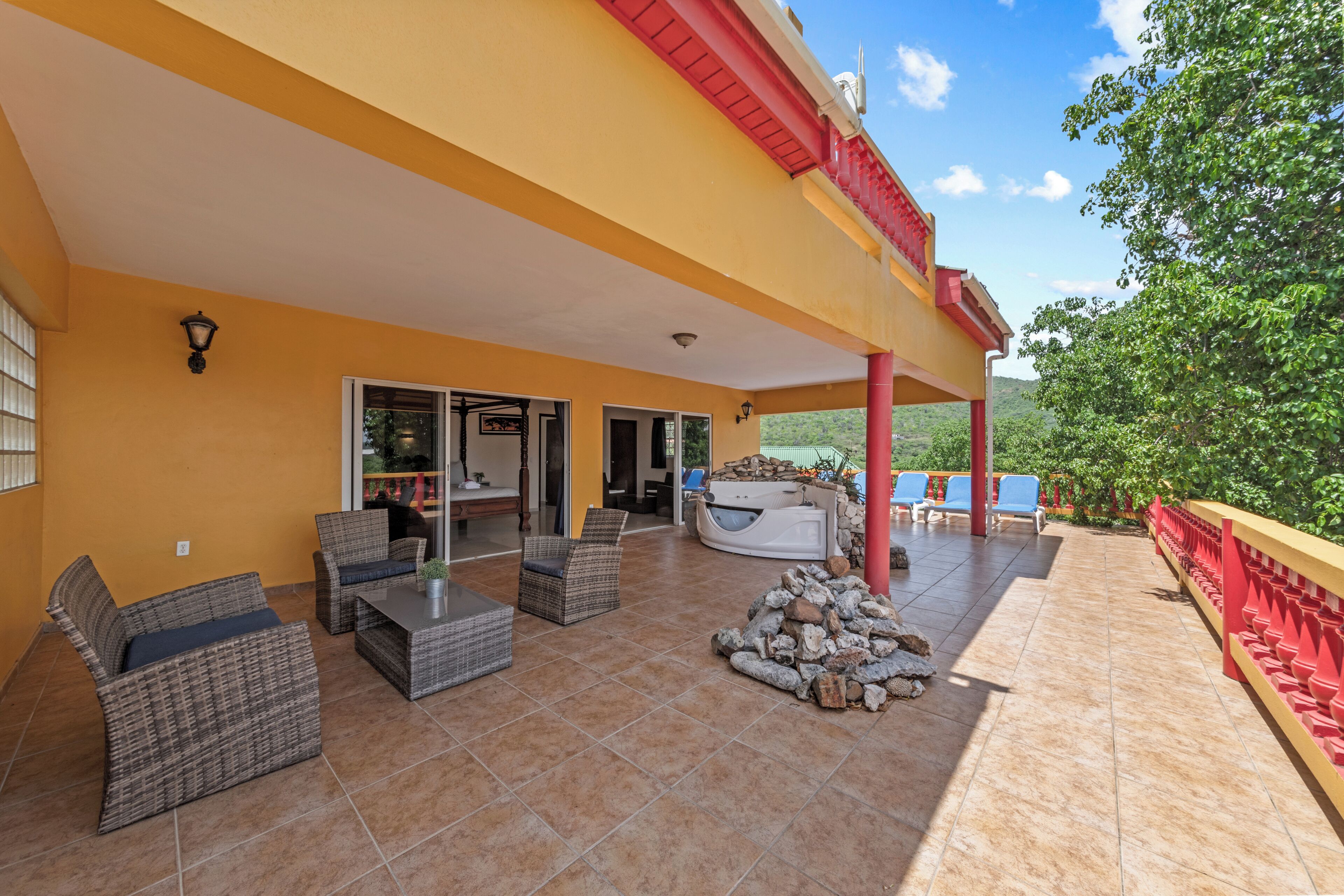 A covered patio with wicker furniture, a stone fire pit, and a view of the surrounding landscape.