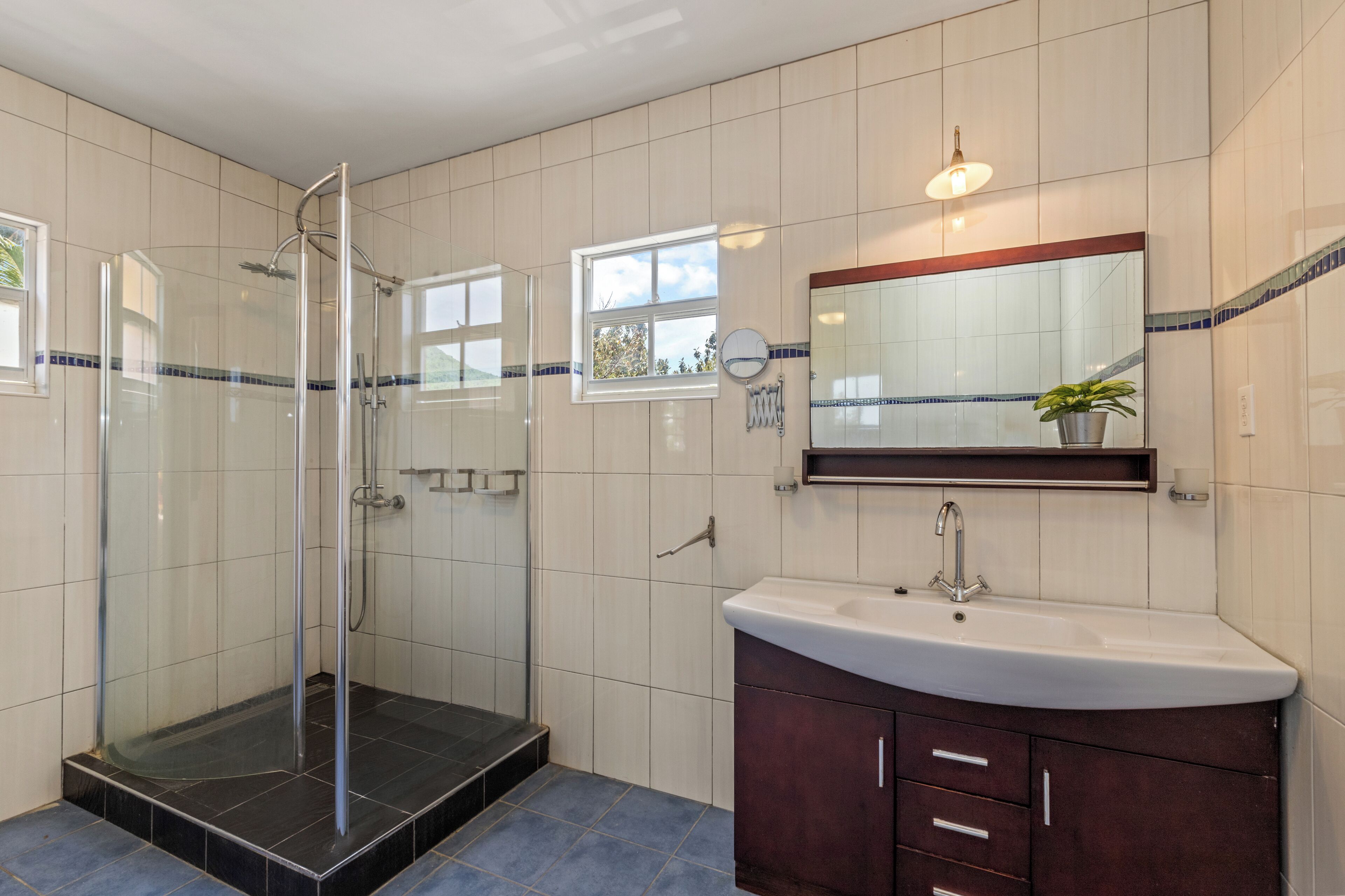 A bathroom with a glass-enclosed shower, a sink with a mirror above it, and a window providing natural light.