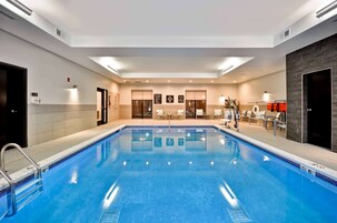 Una piscina con borde de azulejos, una escalera y algunas sillas de descanso.