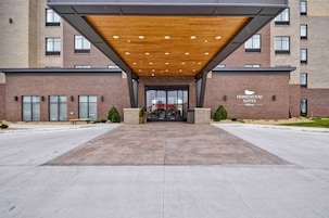 Entrada de un hotel con un corredor cubierto, fachada de ladrillo y un letrero de Homewood Suites Hilton.