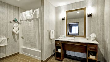 Un baño moderno con bañera, un espejo grande y un tocador con lavabo y toallero.