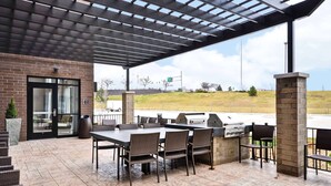 An outdoor patio with a brick wall, a covered seating area, and a grill. - Homewood Suites by Hilton Cincinnati/West Chester (West Chester)