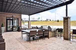 Un patio al aire libre con pared de ladrillo, zona de estar cubierta y una parrilla.