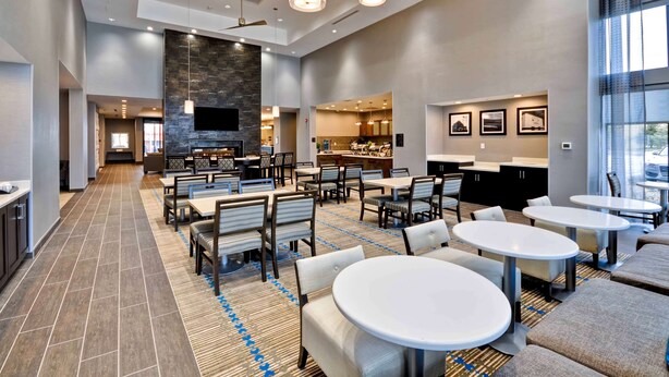 A spacious hotel lobby with a central seating area, a fireplace, and a kitchen in the background. - Homewood Suites by Hilton Cincinnati/West Chester (West Chester)