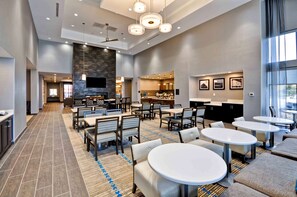 A spacious hotel lobby with a central seating area, a fireplace, and a kitchen in the background. - Homewood Suites by Hilton Cincinnati/West Chester (West Chester)