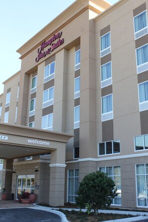 Een hotelentree met een bord waarop "Hampton Inn & Suites" staat en een welkomstbord eronder.