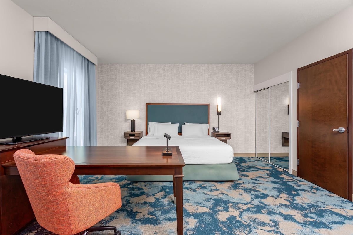 A hotel room with a bed, a desk, a TV, a chair, and a carpet.