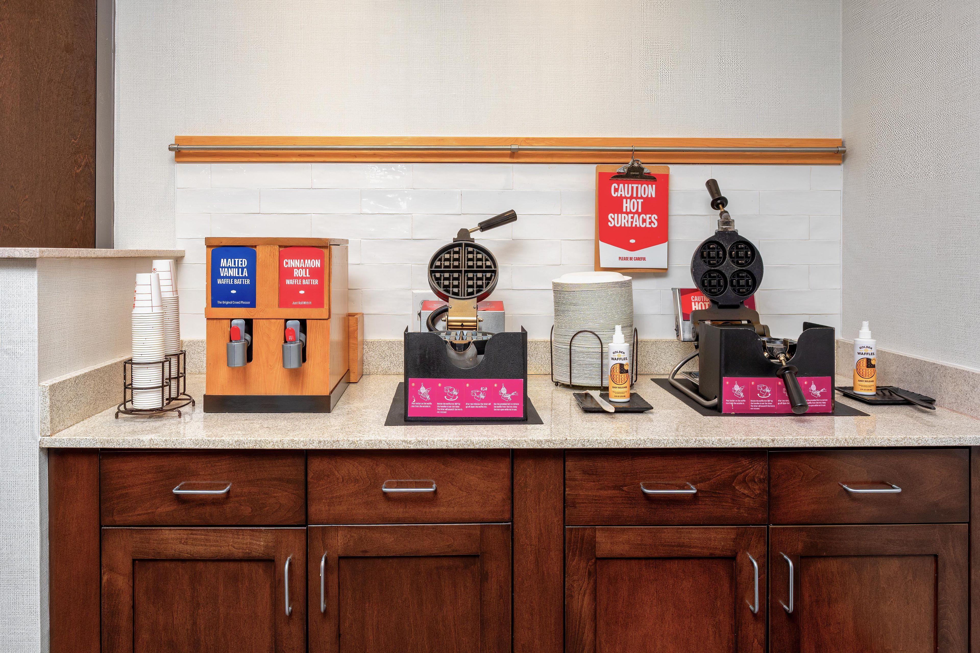 A kitchen counter with waffle makers, waffle batter dispensers, and a caution sign.