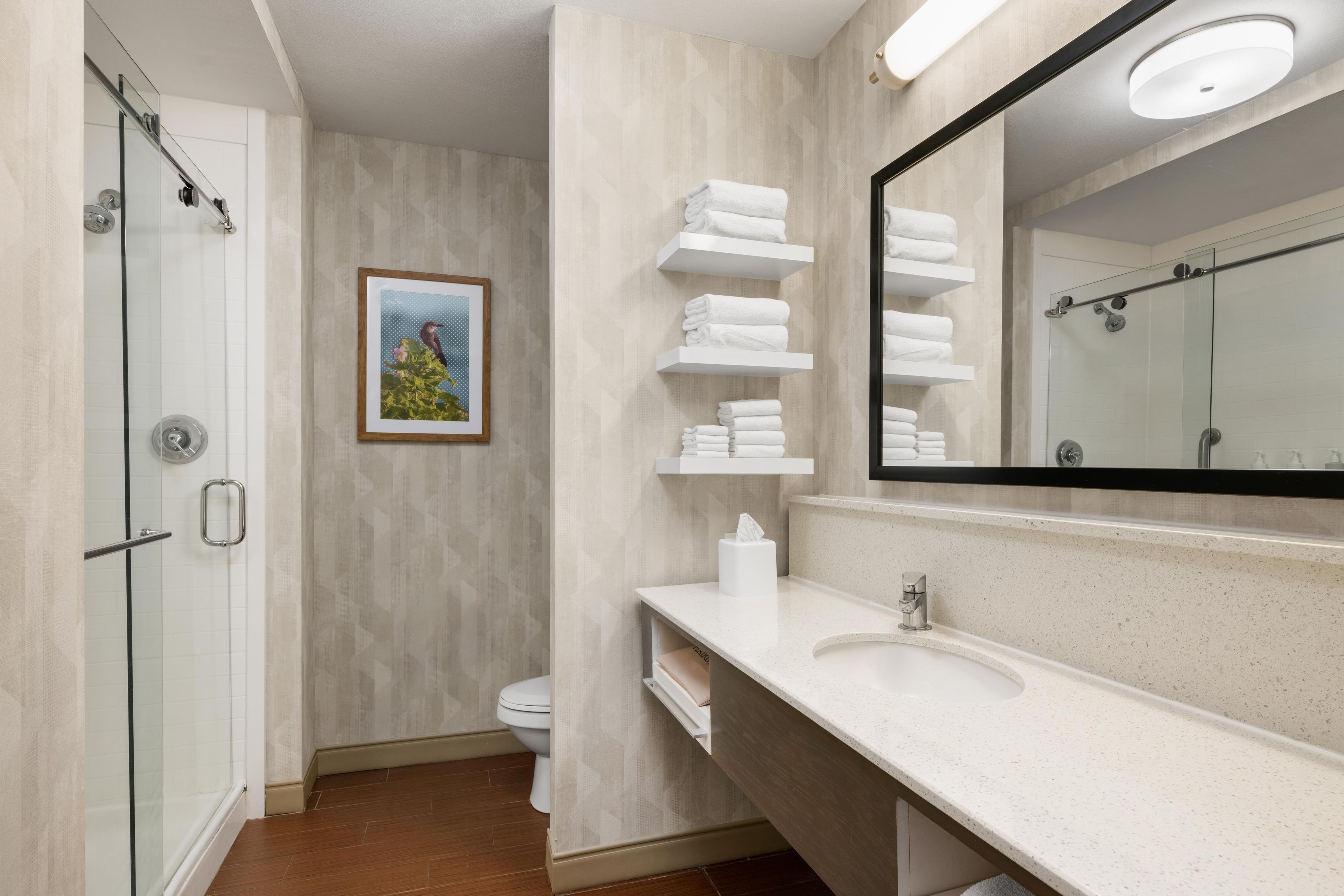 A bathroom with a glass shower enclosure, a toilet, a sink with a mirror, and towel racks.