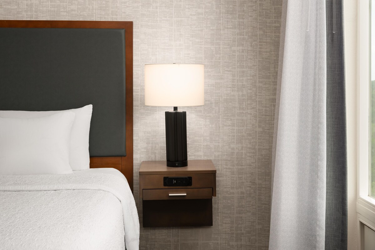 Een keurig opgemaakt bed met hoofdeinde, nachtkastje met lamp, en een muur met een structuur.