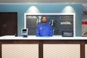 Un mostrador de recepción de hotel con un quiosco digital, un cartel grande con la palabra 'smile' y una insignia de 'Hilton Honors'.